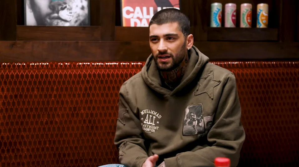 Person sitting in a cozy room with vintage decor, wearing a casual hoodie with graphic patches, engaged in conversation