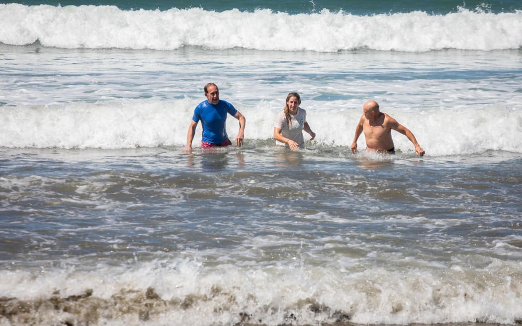 Wellington mayor Andrew Little, left, swims in Lyall Bay after announcing the lifting of a swimming ban.