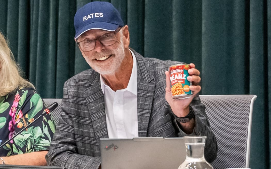 Auckland Mayor Wayne Brown wore a cap with the word 'Rates' on it in a move to mock the governments proposed legislation to cap rates rises. He brought a can of baked beans to the Auckland Council meeting, saying it represents the monthly saving the bill will give to ratepayers.