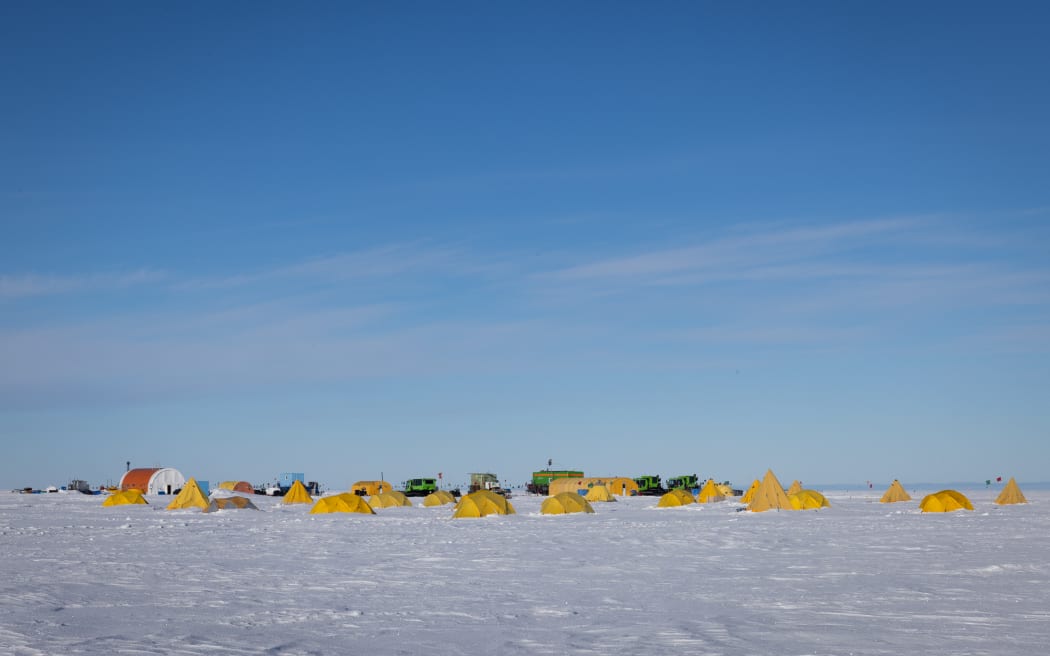 A row of bright yellow tents on the ice in Antarctica, against a bright blue sky.