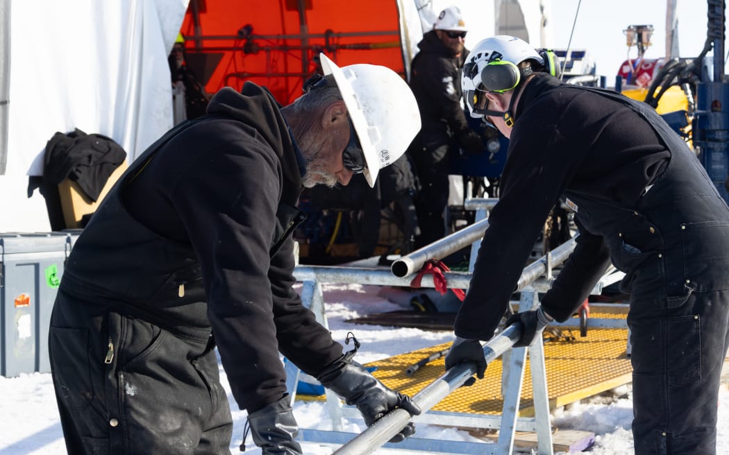 Tony Kingan, wearing overalls and a hard hat, carefully holds a sediment core as it's extruded from the drill pipe.