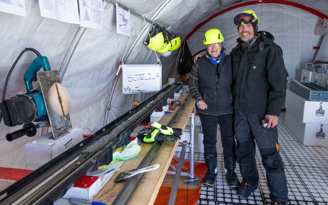 Molly Patterson and Huw Horgan, dressed in warm field gear and neon hard hats, stand inside the drilling tent next to the first sediment core - a dark grey, narrow cylinder of mud.