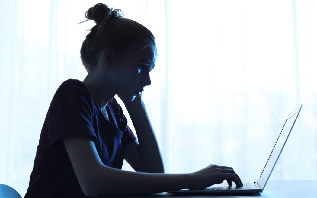 Upset teenage girl with laptop at table indoors. Danger of internet