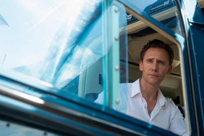 Tom Hiddleston as Jonathan Pine in The Night Manager season 2; in this scene, he is looking out the window of a helicopter, while wearing a white shirt