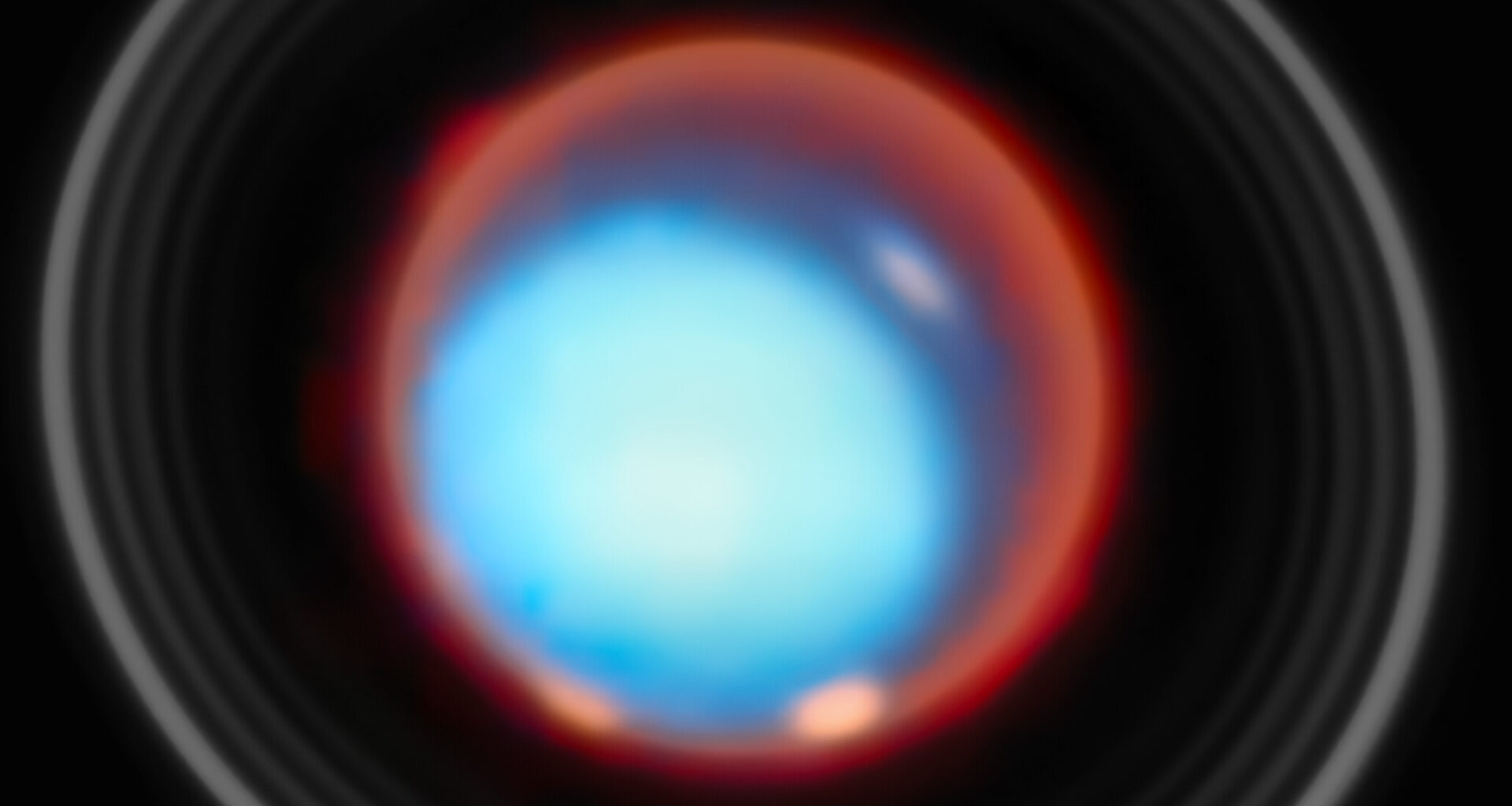 This image shows the planet Uranus set against the blackness of space. The planet appears as a smooth, bright cyan disc at the center, its atmosphere reveals soft, hazy tones of blue. Surrounding the planet is a vivid reddish glow, forming a diffuse halo that contrasts strongly with the cool blue of the planetary disc. Encircling Uranus are several thin, concentric rings, visible as pale gray arcs. Subtle variations in brightness can be seen across the planet’s face, with slightly brighter patches near the limb, hinting at atmospheric structure.