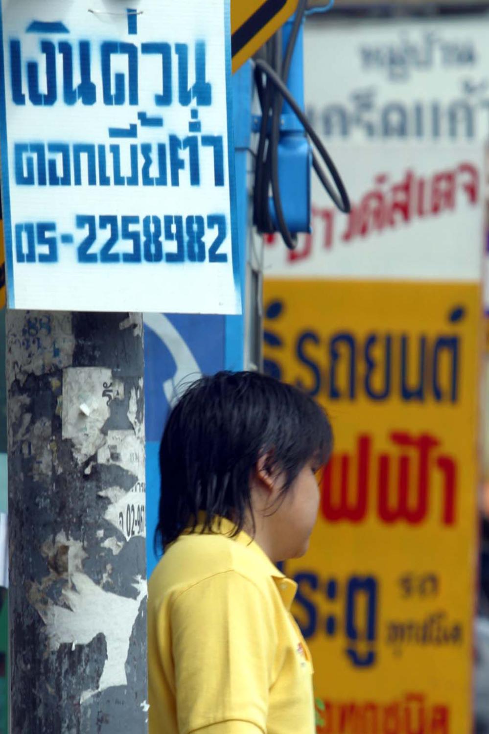 A woman walks past an ad promoting informal loans. A potential rise in informal borrowing is worrisome, particularly amid subdued credit growth in the banking sector and a declining household debt-to-GDP ratio. Weerawong Wongpreedee