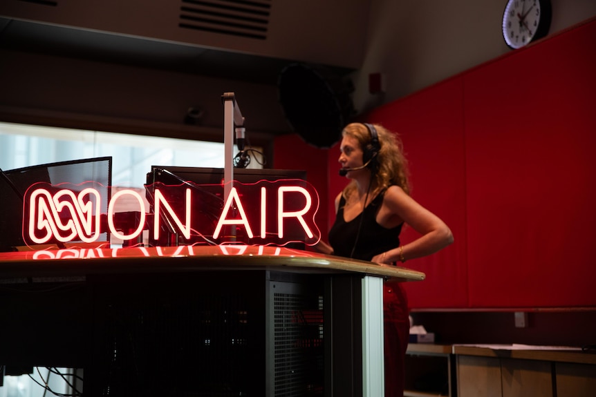 A woman stands next to an On Air side on a desk