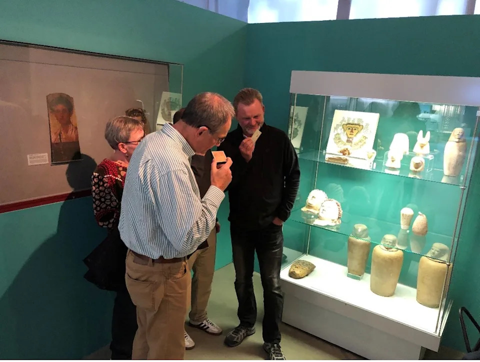 three people in a museum exhibit. two are smelling cards