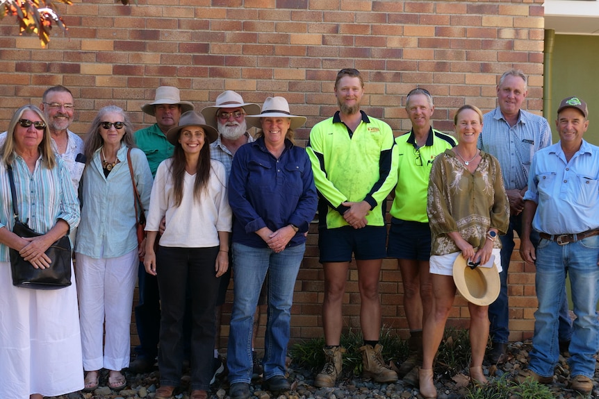 A group of people stand, smiling, outside a building. 
