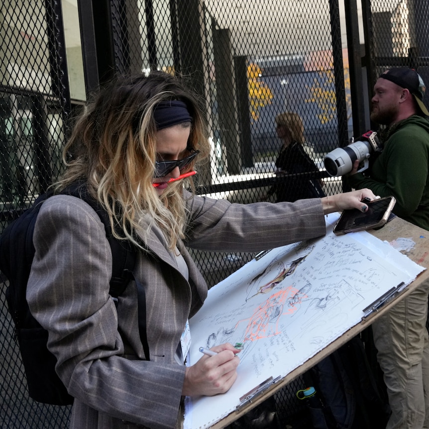 An artist holds out a large sheet of paper and sketches. 