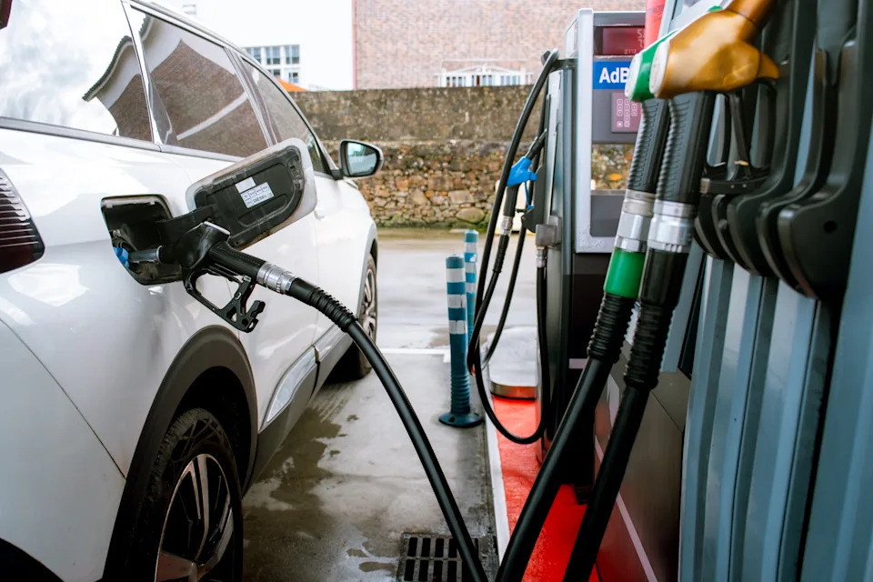 Car at gas station with fueling nozzle inserted, fueling in progress. Part of a gas pump with nozzles is visible in the foreground