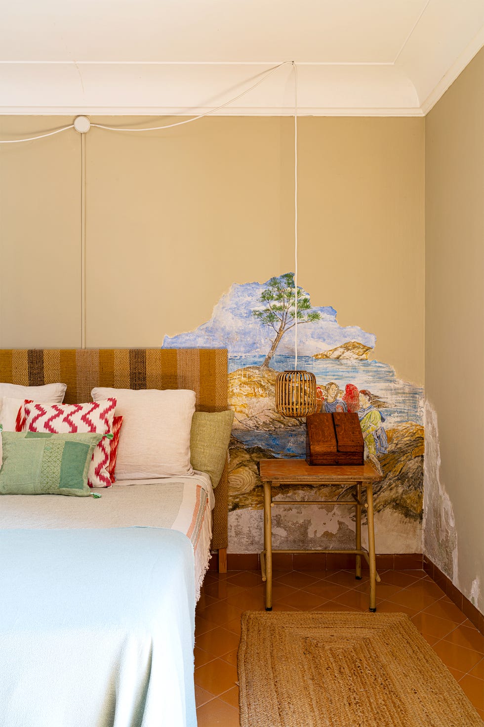 Cozy bedroom featuring a bed with colorful pillows and a rustic painting on the wall.