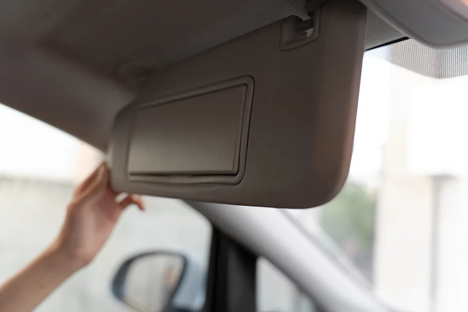 A person adjusts a sun visor inside a car, with a partial view of the outside through the window