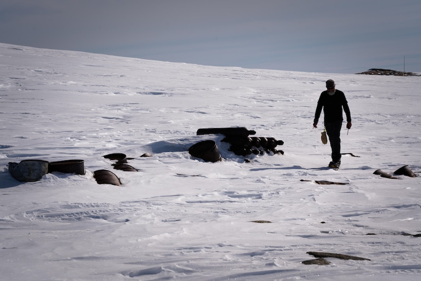 A person walking around wreckage in the snow.