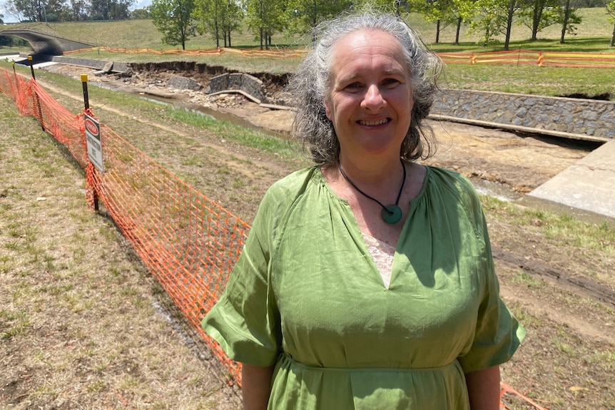 A woman with  long hair stands in front of a badly damaged concrete floodway.