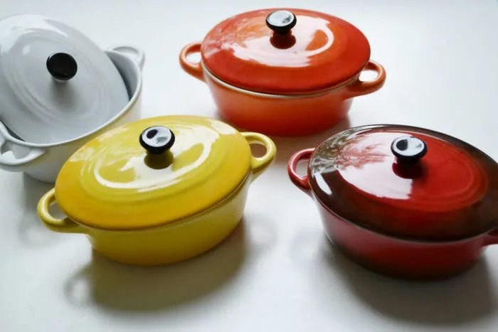 Four enameled cast iron pots with lids are arranged on a table. Each pot is a different color, illustrating options for kitchenware shopping