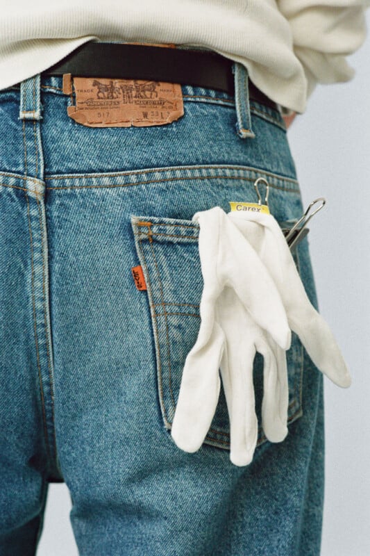 A person wearing blue jeans with a white glove attached to the back pocket using a binder clip labeled "Carex." The person’s torso and waist are partially visible, wearing a light sweater.