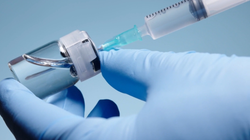Gloved hand drawing vaccine from a vial into a syringe