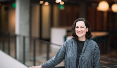 A dark-haired woman poses by a balcony in a gray cardigan sweater.