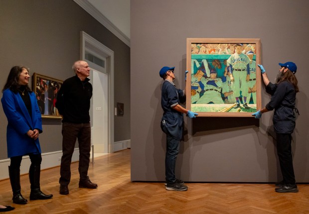 Specialists Tim Roby, center, and Chris Shepherd install Norman Rockwell's painting "The Dugout," portraying the Cubs, Feb. 10, 2026, at the Art Institute of Chicago. Former Gov. Bruce Rauner, second from left, and his wife, Diana, gifted the painting to the museum after hanging it in their home for the past 19 years. (Brian Cassella/Chicago Tribune)