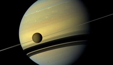 A view of Saturn with its rings creating a shadow on its body. A moon is in the foreground.