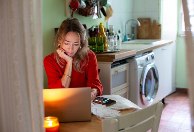 Woman sitting at kitchen table, using laptop and sorting through paperwork