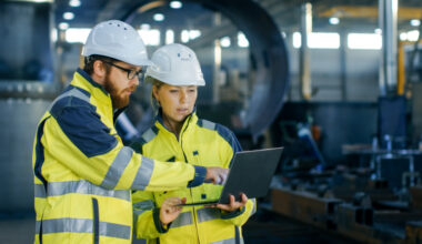 man and woman wearing protective helmets in a factory