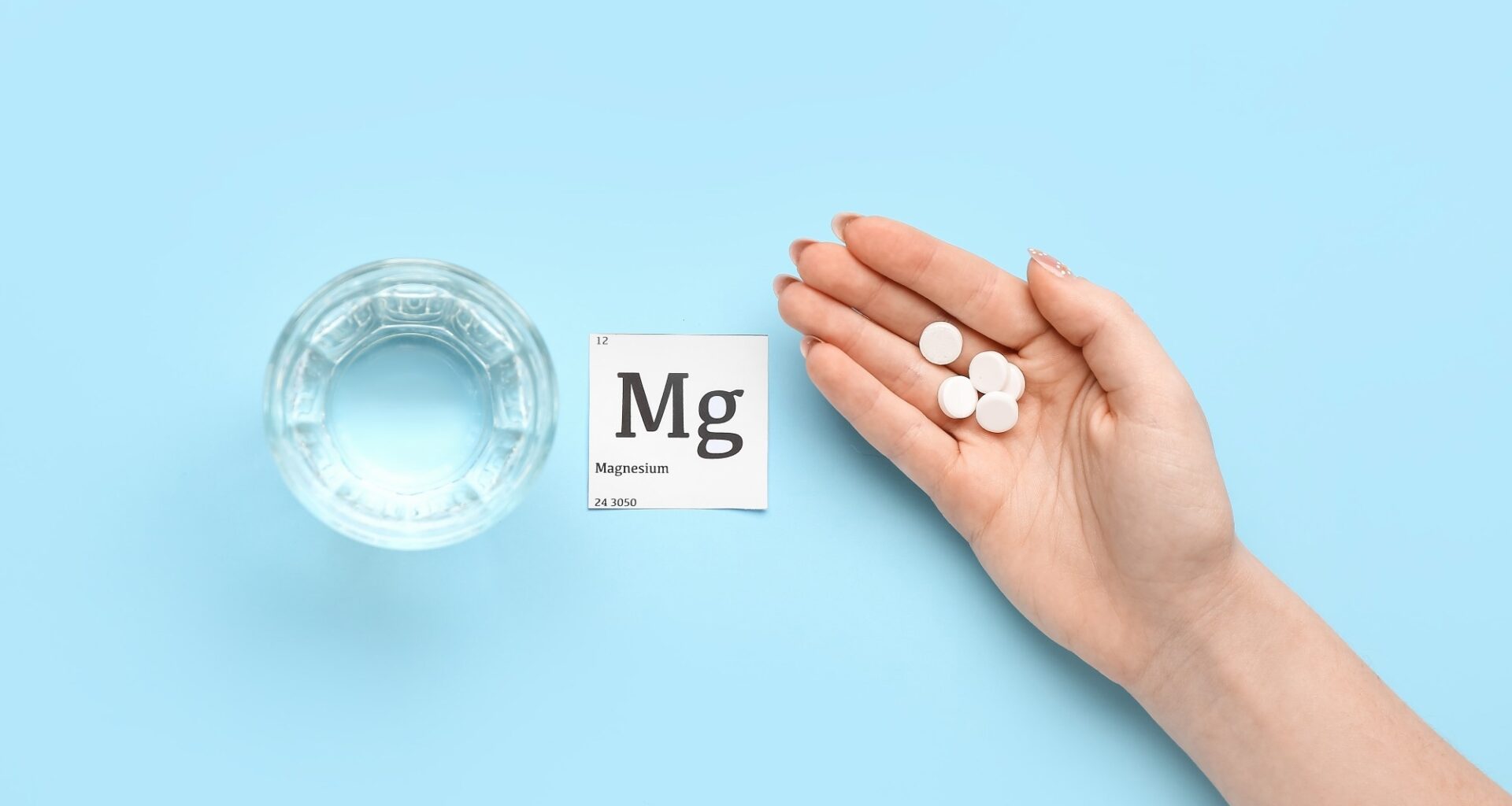 Female hand with magnesium pills and glass of water on blue background