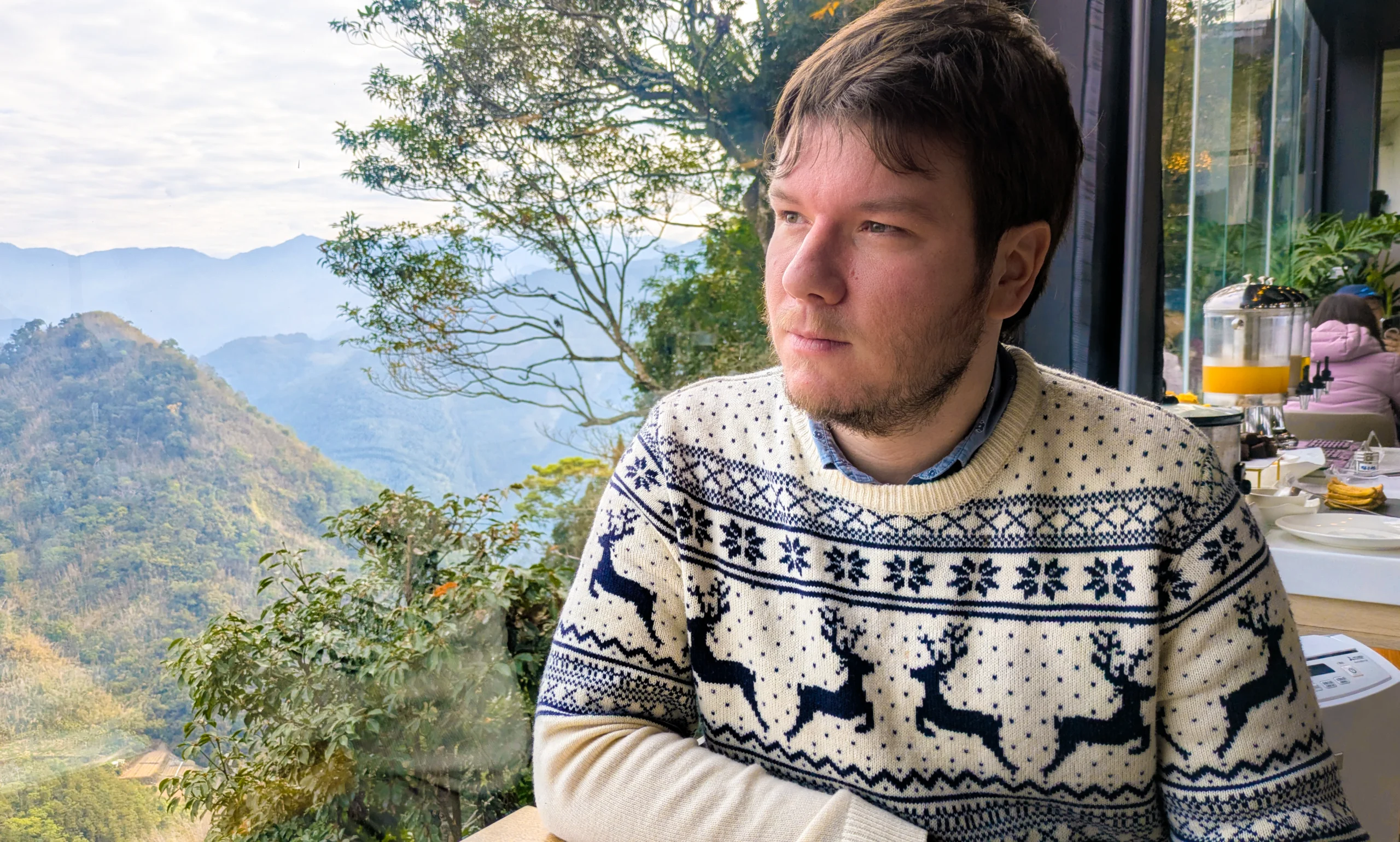 Portrait of a man sitting next to a window with a view of mountains.
