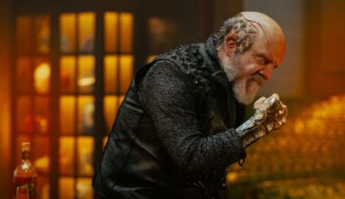 a humanoid alien with x's and o's shaved into the side of his head and a raised cranium makes a fist and an angry face