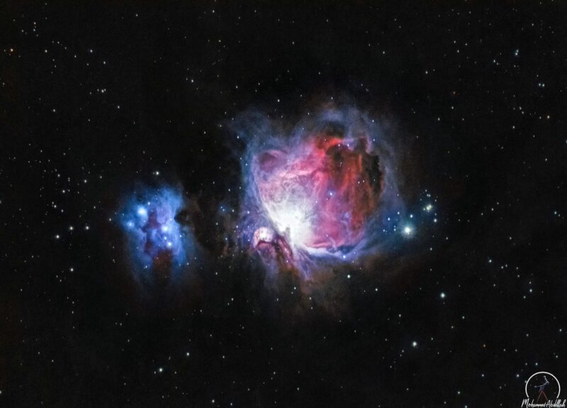 Large swirls of bright, blue and red nebulosity over a background of prolific stars.