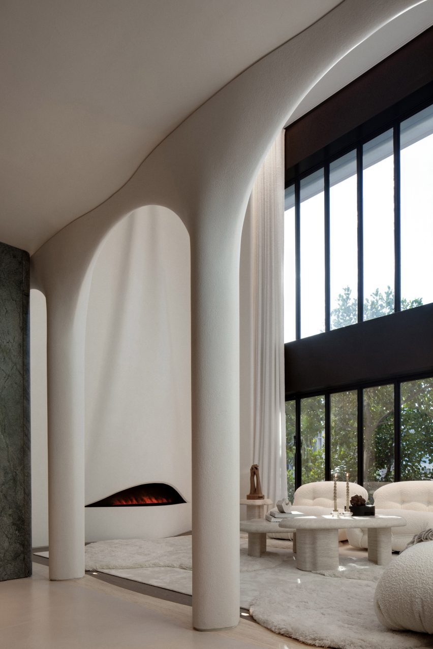 A living room with a fireplace with white walls, white furniture and tall windows on the right hand side of the image.