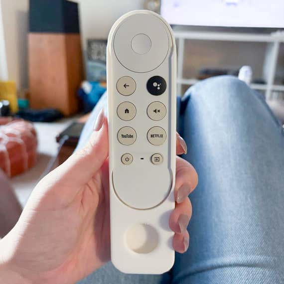 A person's hand holding a tv remote which is fit into a custom-made plastic sleeve that has an AirTag-shaped hole at the bottom.