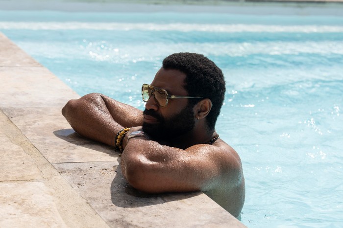 Nicholas Pinnock stars in Two Weeks in August; in this scene, he is in a swimming pool, resting his arms on the edge and looking ahead of him