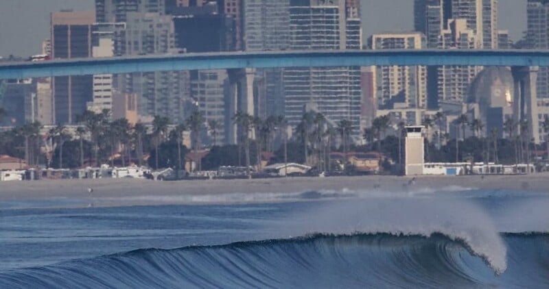 A large wave in the ocean with a bridge in the background.