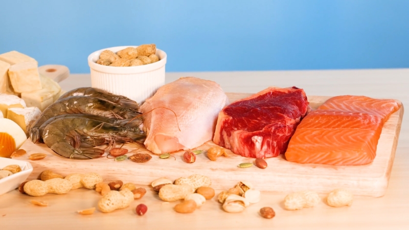 Raw meat, fish, shrimp, cheese, and nuts arranged on a wooden board as common protein sources