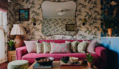 an eclectic, small living room in london with patterned wallpaper and a large dark pink couch with patterned pillows