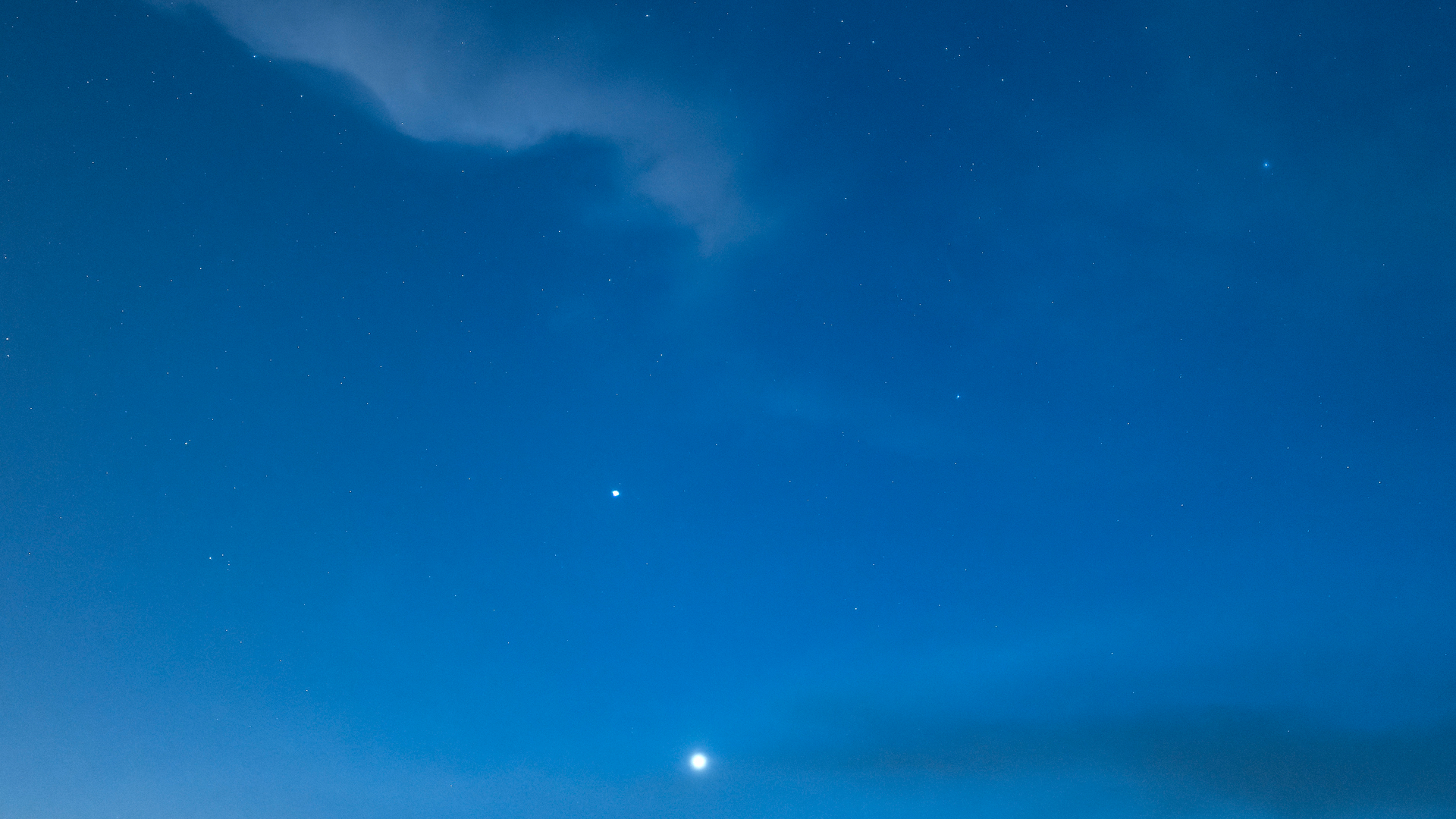 A pale blue night sky with a streak of white clouds and glowing dots of planets and stars in the night sky