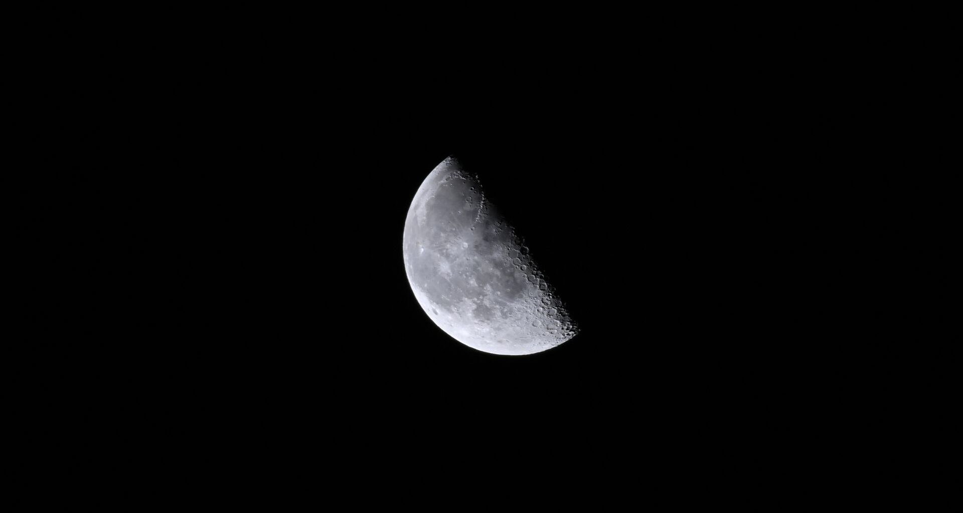 A close up of the moon in the darkness of space, with its top right half obscured in shadow