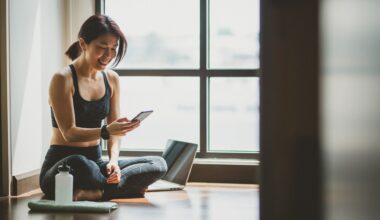 Woman looking down at phone smiling with water bottle and laptop