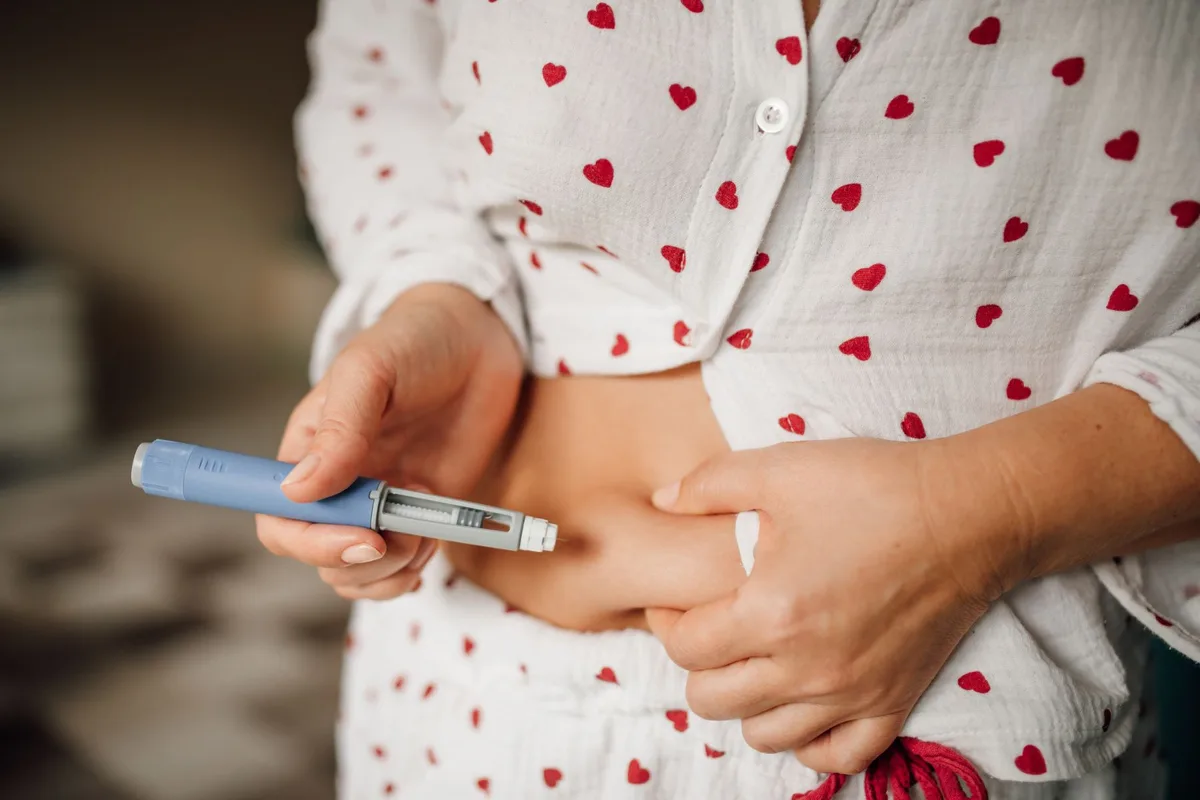 Someone in love-heart patterned pyjamas injects themselves with a weight-loss drug, such as Ozempic, with a blue pen