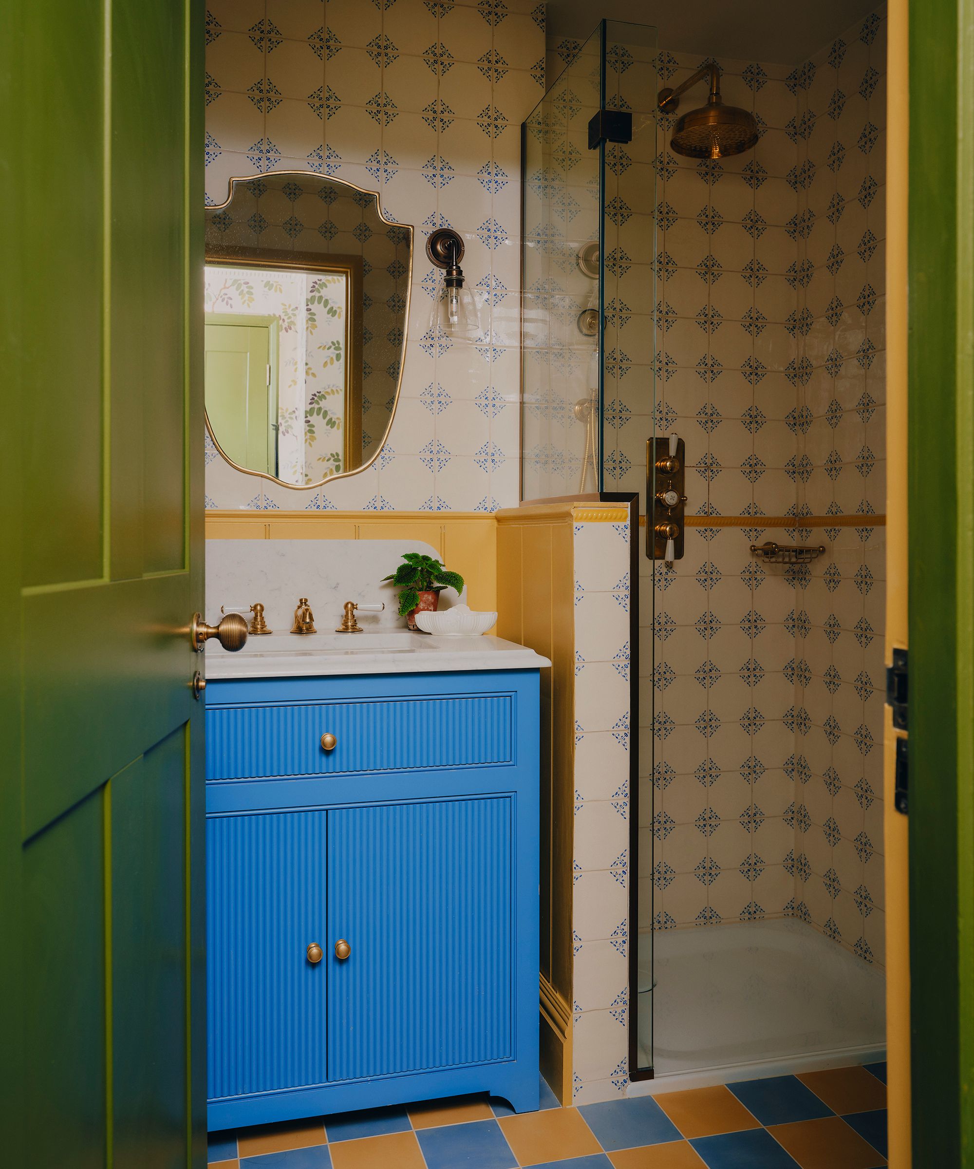 a small bathroom with orange and blue floor tiles, a bright blue vanity unit, delft wall tiles and green woodwork