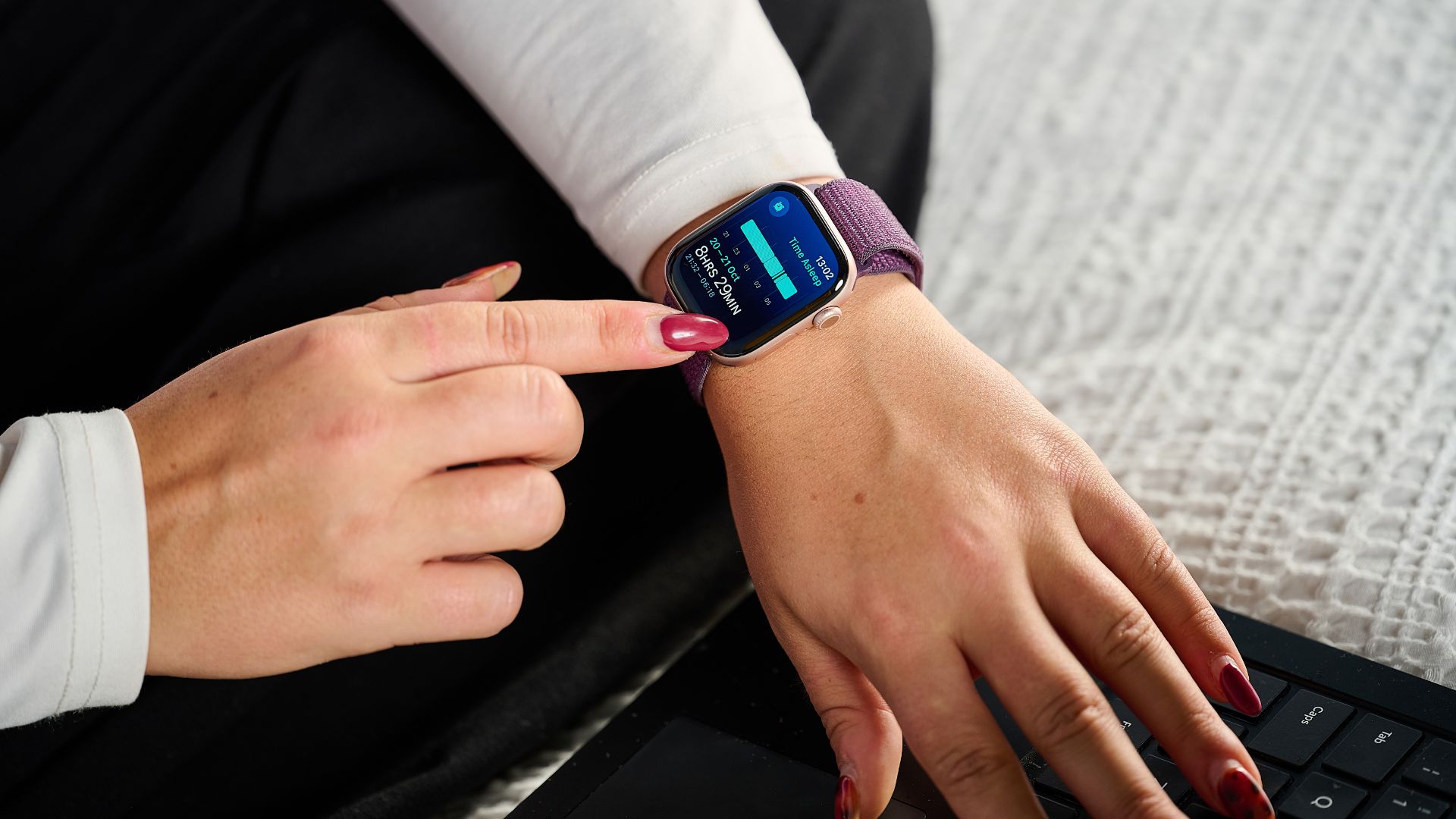 A young woman looks at her wrist, where she is wearing an Apple Watch displaying sleep tracking data.