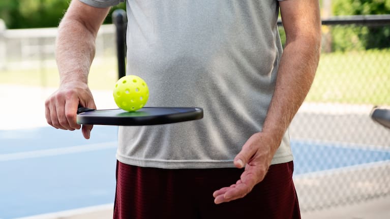 A man holds a pickleball racket and ball.