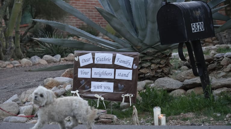 Lit candles next to a sign from neighbors supporting the Guthrie family outside of Nancy Guthrie’s house