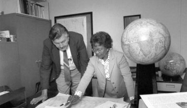 a woman in a suit points at a map on a table next to a globe