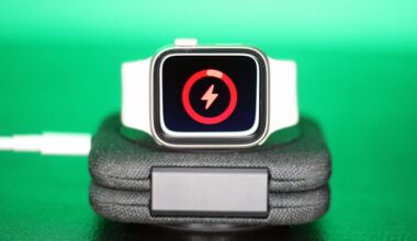 Apple Watch with white band charging on a dock, with a screen indicating low battery