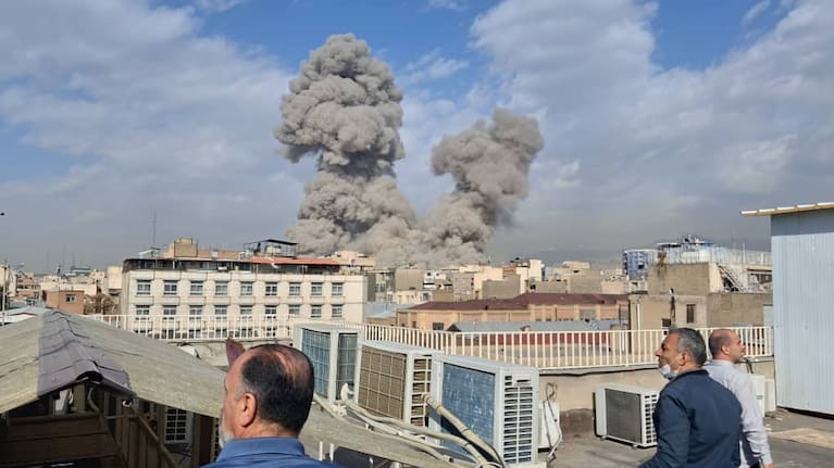 People watch as smoke rises on the skyline after an explosion in Tehran, Iran.