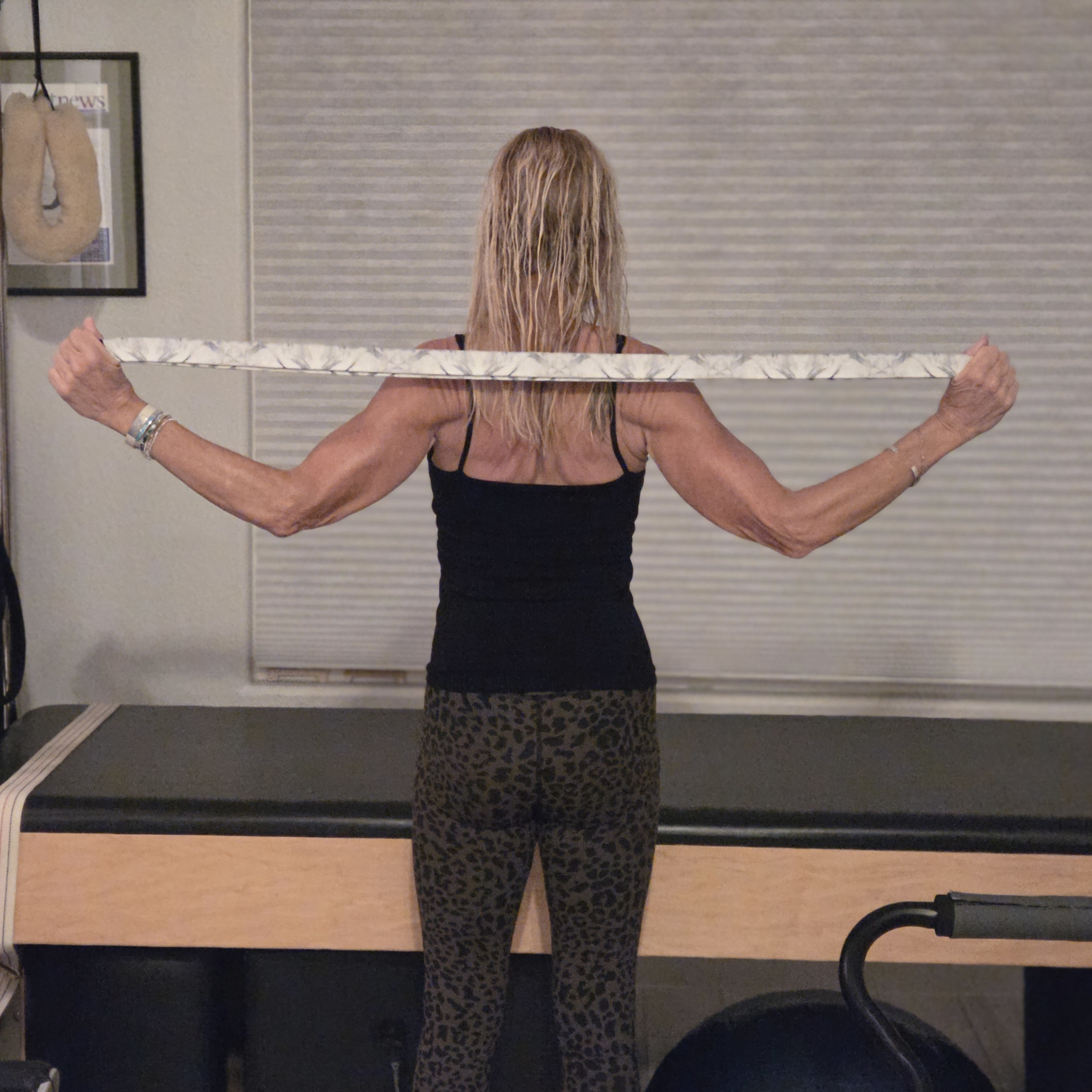 Woman stretching with yoga strap in front of a Pilates reformer bed