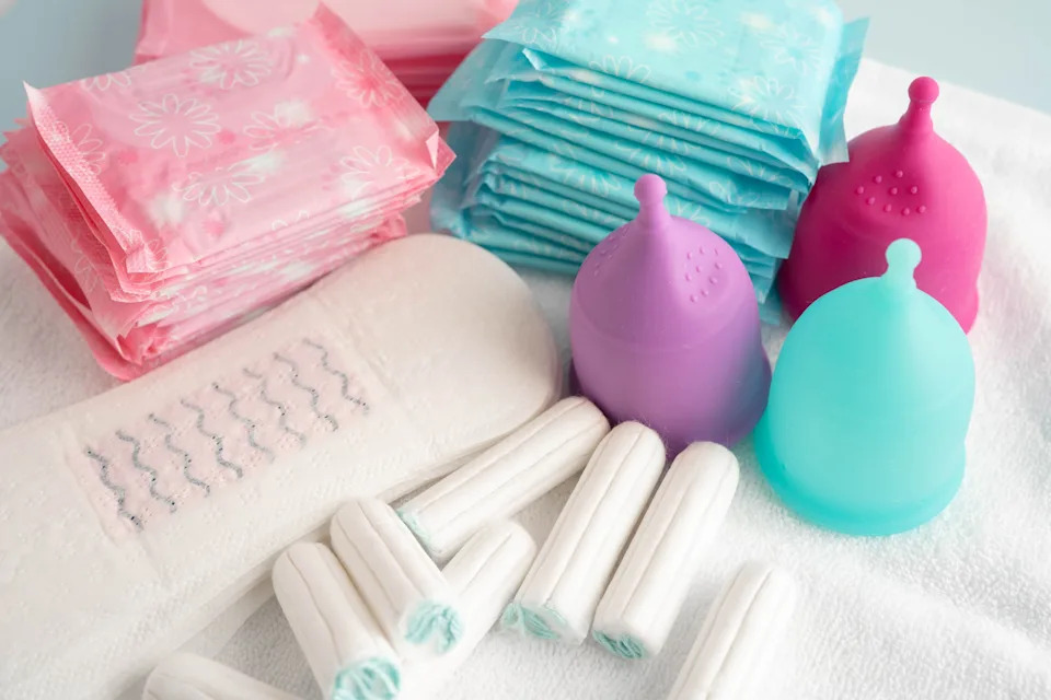 Various period products, including pads, tampons, and menstrual cups, are displayed on a surface